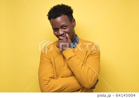 Young african american man in yellow sweater contemplating a plan hiding smile. Young african american man in yellow sweater contemplating a plan hiding smile. 64145004