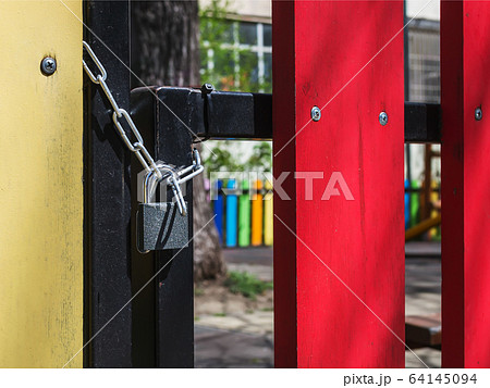 Padlock locks the gate of a fenced outdoor playground on a sunny day. 64145094