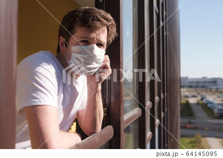 man with grippe looking through window and wearing mask protection 64145095