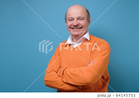 Smiling mature casual man in orange sweater isolated on blue background Smiling mature casual man in orange sweater isolated on blue background 64145753