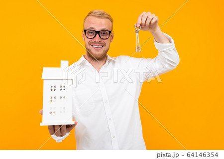 realtor guy holds a house model in his hand on a yellow background with copy space 64146354
