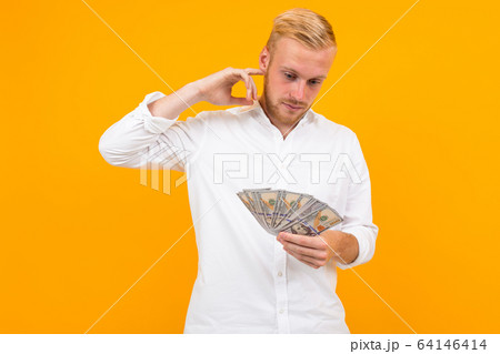 man in a white shirt ponders what to spend earned money on a yellow background with copy space 64146414