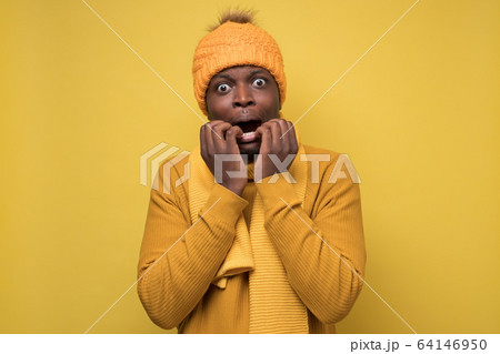 African american man in yellow scarf and hat biting nails and being scared African american man in yellow scarf and hat biting nails and being scared 64146950