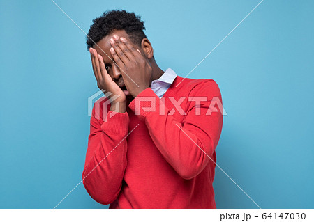 man is very upset, he covered his face with his hands on blue background man is very upset, he covered his face with his hands on blue background 64147030