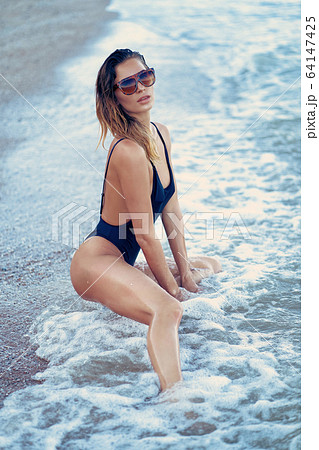 portrait of beautiful sexy caucasian sunbathed woman in leopard print sunglasses with long hair in swimsuit lying on summer beach 64147425