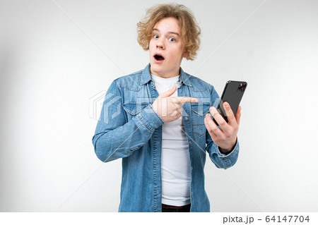 blond man with wavy white hair and a surprised face shows a finger on his phone in his hands on a 64147704