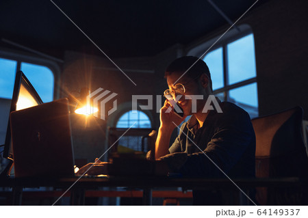 Man working in office alone during coronavirus or COVID-19 quarantine, staying to late night 64149337