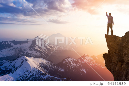 Adventurous Man Hiker With Hands Up on top of a Steep Rocky Cliff 64151989