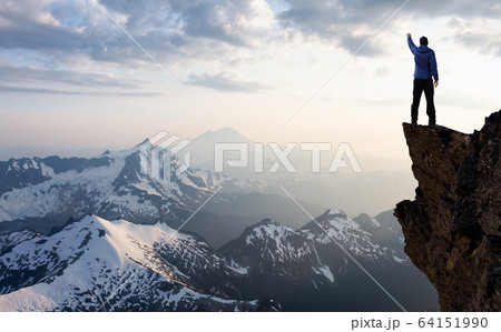 Adventurous Man Hiker With Hands Up on top of a Steep Rocky Cliff 64151990