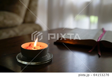 Burning candle with book, curtain and couch at the 64153276