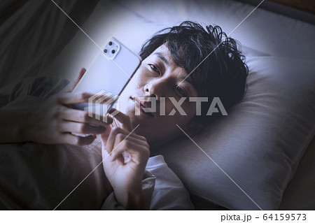 寝ながらスマートフォンを操作する男性 64159573