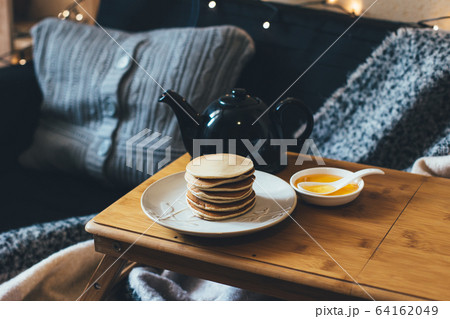 Pancakes with honey on wooden tray in cozy room. 64162049