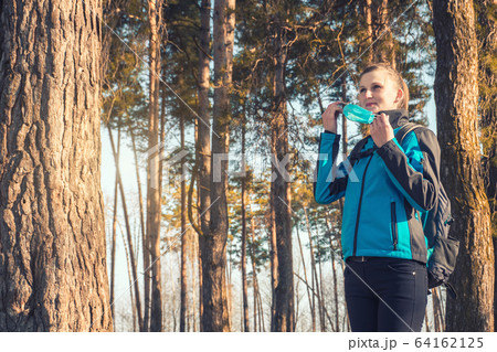 young woman in medical mask walks in a spring pinewood. Spring. young woman in medical mask walks in a spring pinewood. Spring. 64162125