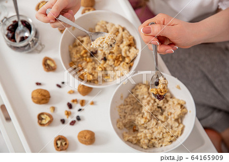 Happy mom and daughter have healthy breakfast in bed on a sunny morning. Oatmeal porridge with nuts Happy mom and daughter have healthy breakfast in bed on a sunny morning. Oatmeal porridge with nuts 64165909
