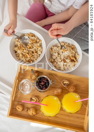 Happy mom and daughter have healthy breakfast on bed in a light bedroom on a sunny morning. Orange Happy mom and daughter have healthy breakfast on bed in a light bedroom on a sunny morning. Orange 64165924