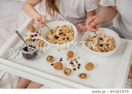 Happy mom and daughter have healthy breakfast on bed in a light bedroom on a sunny morning. Oatmeal Happy mom and daughter have healthy breakfast on bed in a light bedroom on a sunny morning. Oatmeal 64165979