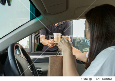 Woman in protective mask taking coffee at drive thru during covid-19 outbreak. 64168008
