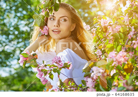 Beautiful young woman walking near the blossoming 64168635