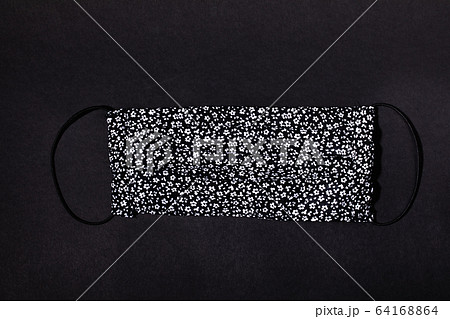 Textile handmade medical mask with black and white floral pattern on black. Mask - means of protection against virus during epidemic. Pandemic Covid-2019. Self-safety during quarantine. Top view. Textile handmade medical mask with black and white floral pattern on black. Mask - means of protection against virus during epidemic. Pandemic Covid-2019. Self-safety during quarantine. Top view. 64168864