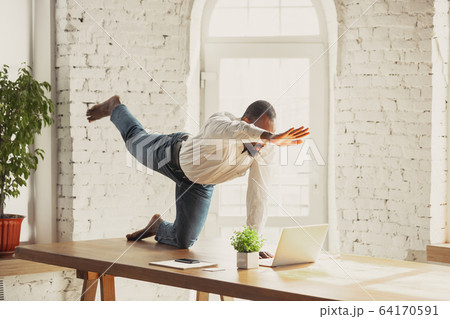 Young african-american man doing yoga at home while being quarantine and freelance working 64170591