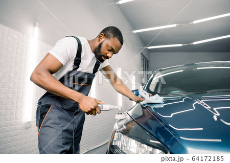 African man professional car detailing worker, polishes a blue car with a polisher and microfiber cloth. Car detailing concept 64172185