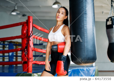 Sporty young woman wearing boxing gloves posing in gym Sporty young woman wearing boxing gloves posing in gym 64173550