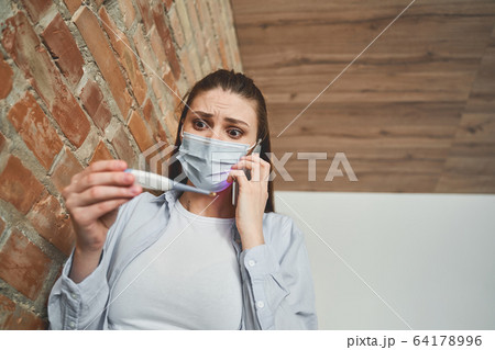 Scared young Caucasian female holding a thermometer Scared young Caucasian female holding a thermometer 64178996
