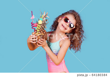 Beautiful girl in colorful swimsuit and sunglasses holding pineapple cocktail 64180384