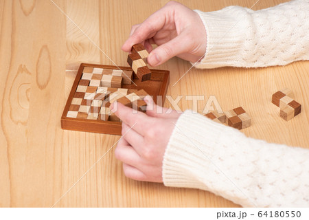 Girl in a light sweater is trying to assemble a polymino puzzle. 64180550