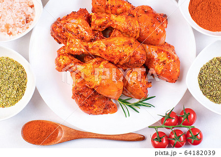 Raw marinated chicken drumsticks.Chicken legs in a marinade with spices and tomatoes on a white plate. 64182039