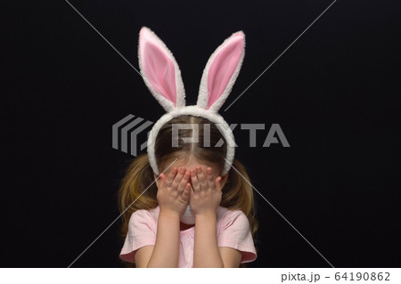 Concept of coronavirus and air pollution. A little girl wears a mask for protection and an Easter Bunny ears costume. Worried about crying about a ruined holiday. A distressed child. Meeting of Easter 64190862