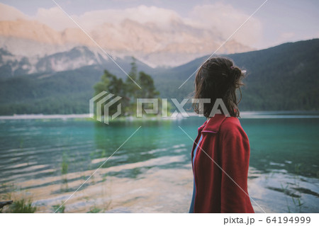 Germany, Bavaria, Eibsee, Young woman standing at by Eibsee lake in Bavarian Alps and looking at view 64194999
