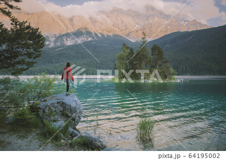 Germany, Bavaria, Eibsee, Young woman standing on rock by Eibsee lake in Bavarian Alps 64195002