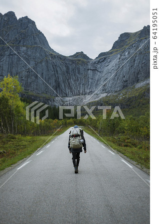 Norway, Lofoten Islands, Backpacker walking down road in mountain landscape 64195051