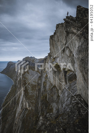 Norway, Senja, Man standing on the edge of steep cliff on top of Segla mountain 64195052