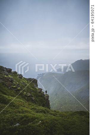 Norway, Lofoten Islands, Reine, Man looking at view from Reinebringen mountain during rain 64195071