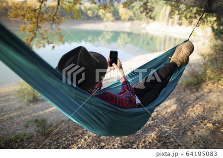 Italy, Man lying in hammock near lake and using smart phone Italy, Man lying in hammock near lake and using smart phone 64195083