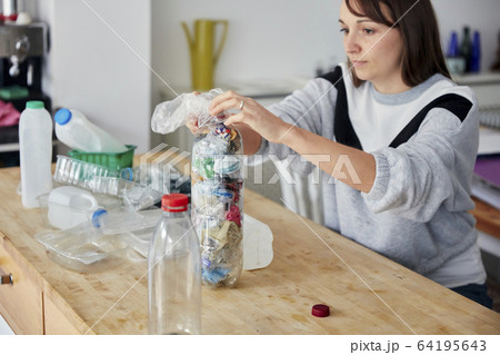 Woman stuffing soft waste plastics into large plastic bottle to make an ecobrick for use as a building block 64195643