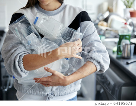 Woman holding armful of used plastic containers in kitchen 64195673