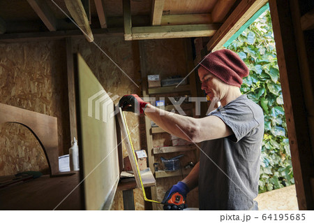 Carpenter using tape measure in shed 64195685