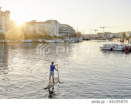 Man standing on paddleboard on river at dawn, shot from behind 64195870