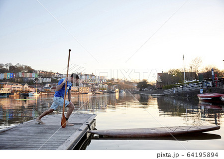 Man holidng paddle stretching legs on riverside jetty before using paddleboard Man holidng paddle stretching legs on riverside jetty before using paddleboard 64195894