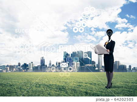 Camera headed woman standing on green grass against modern citys 64202505