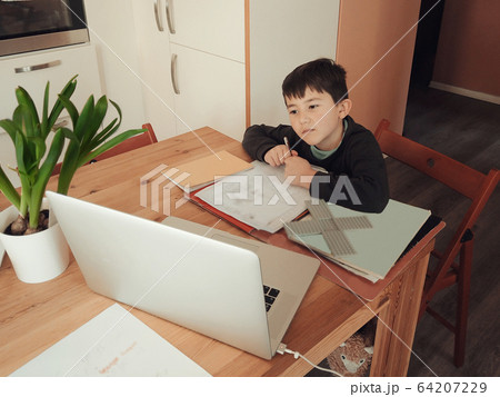 young Caucasian boy following class work online on a laptop computer 64207229