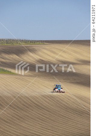Tractor with seed drill in early spring landscape 64211971