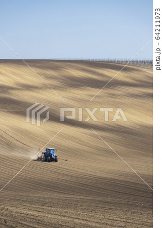 Tractor with seed drill in early spring landscape 64211973