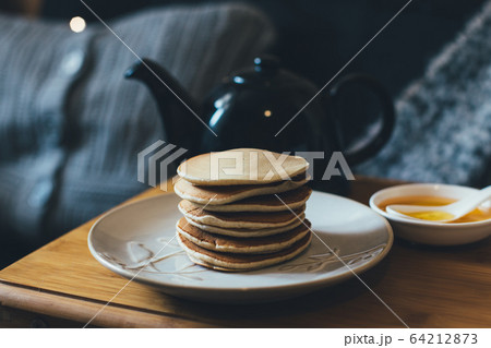 Pancakes with honey on wooden tray in cozy room. Pancakes with honey on wooden tray in cozy room. 64212873
