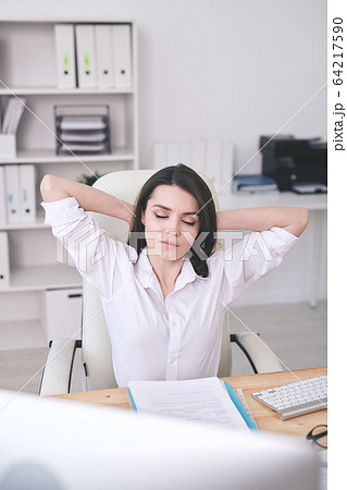 Young serene female office manager relaxing in armchair by desk Young serene female office manager relaxing in armchair by desk 64217590