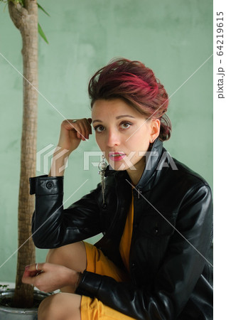 Glam rock style look of a beautiful girl with dark pink hair and mohawk wearing yellow dress and black leather jacket, close-up female portrait 64219615