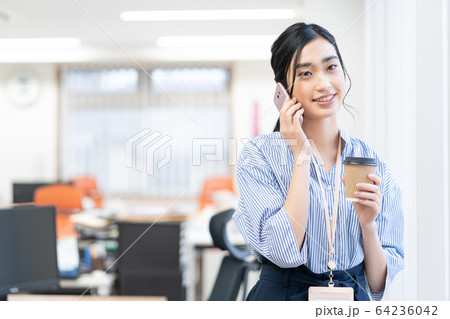 オフィスで飲み物を飲みながらスマホで話をする若い女性社員 64236042